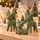 Kit 3 renas de Natal decorativas, cor Verde, em frente a uma vila de Natal iluminada